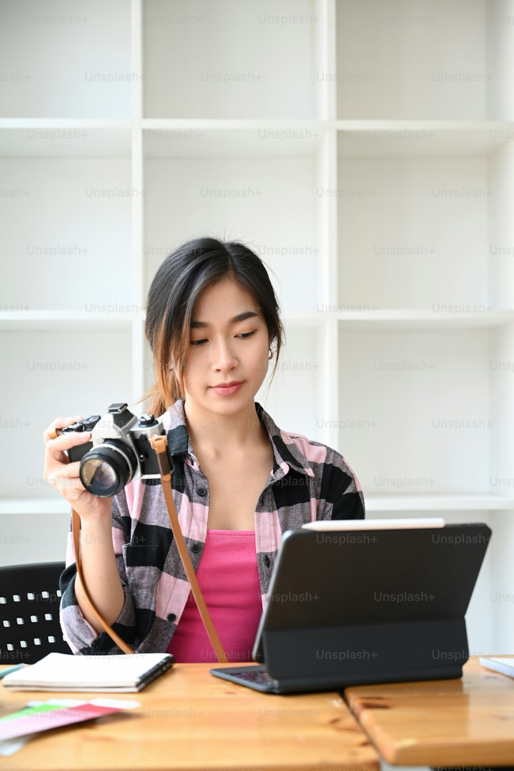 Portrait of female photographer holding her camera and working on computer tablet at modern office.