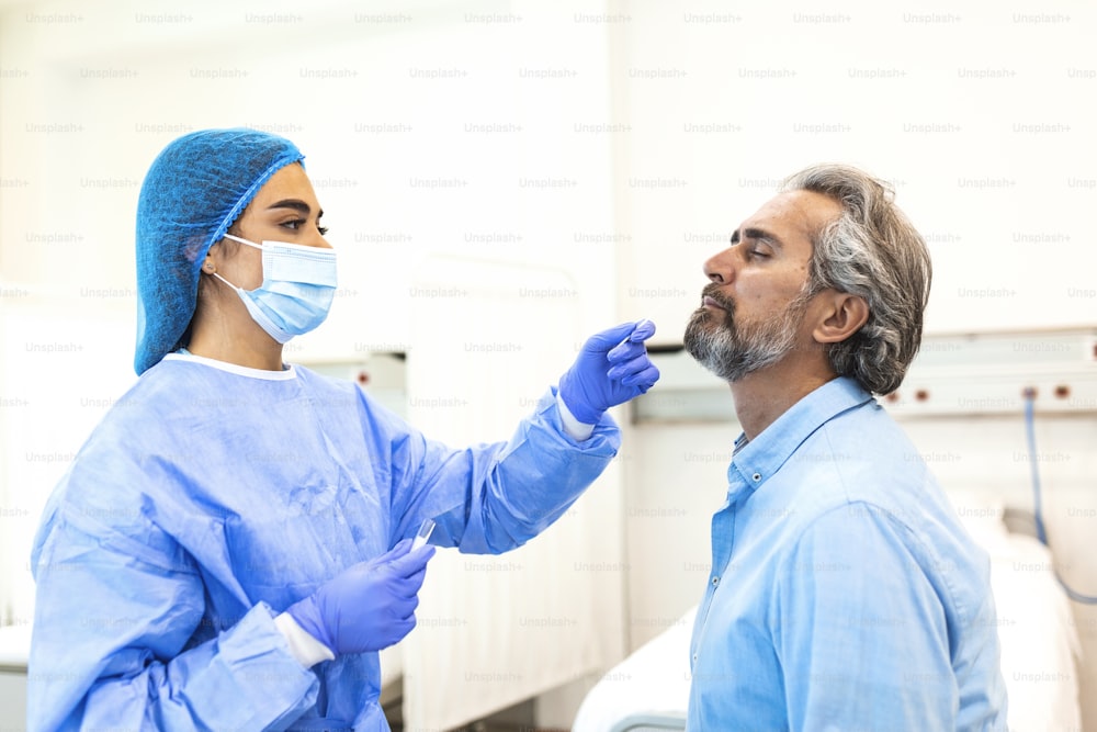 Primo piano del medico di base esegue il test PCR del tampone del coronavirus mentre indossa una maschera protettiva per il viso durante la pandemia di covid-19. Giovane infermiera con maschera chirurgica che prende il tampone nasale per Covid-19