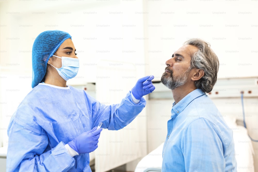 Nahaufnahme eines Hausarztes führt Coronavirus-Abstrich-PCR-Test durch, während er während der Covid-19-Pandemie eine Gesichtsschutzmaske trägt. Junge Krankenschwester mit OP-Maske nimmt Nasenabstrich für Covid-19