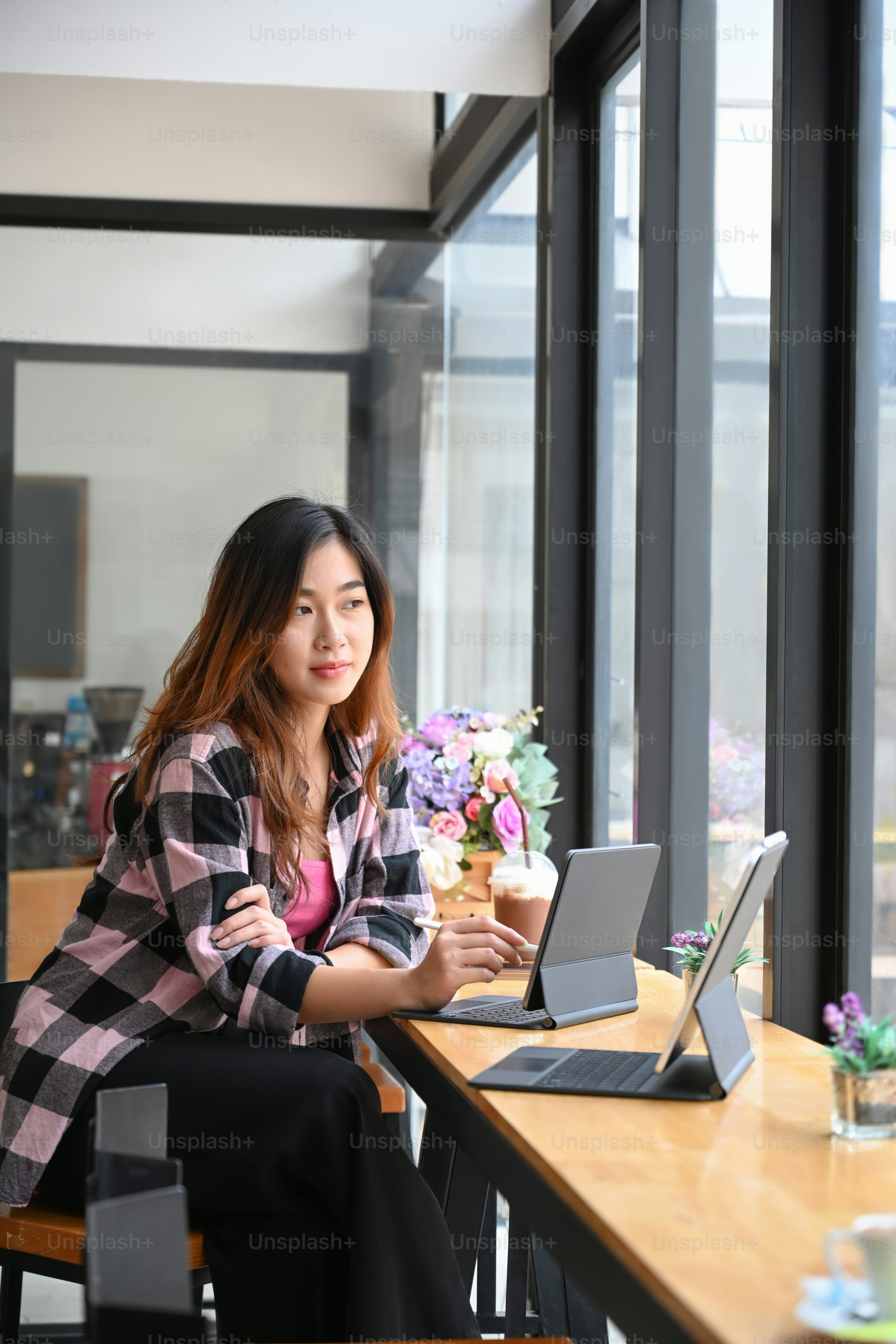 Portrait of thoughtful young woman sitting in coffee shop with her computer tablet and looking out of window.