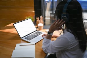 Side view of young woman designer wearing head phone and working on laptop computer.