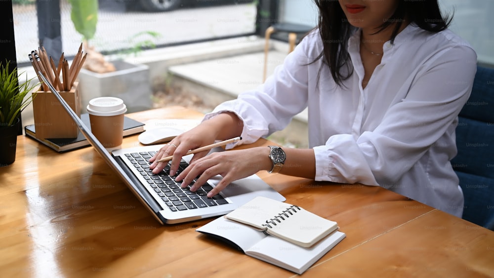 Foto recortada de manos de mujer de negocios escribiendo en la computadora portátil en el escritorio de la oficina.