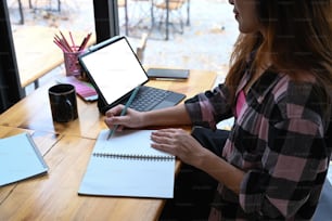 若い女性デザイナーがデジタルタブレットで作業し、ノートにメモを取っている様子を描いている。
