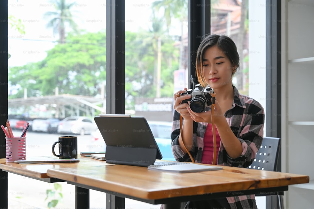 Jovem fotógrafa verificando foto em sua câmera enquanto estava sentada no escritório moderno.