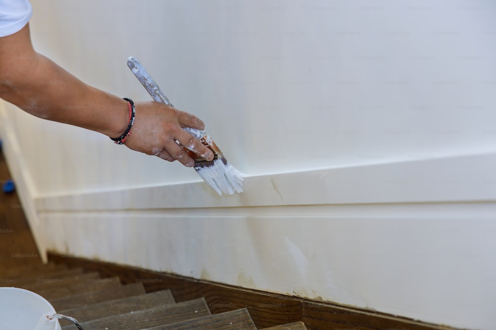 Painter hands with painting the wood molding trim on corners edge on stairs with brush