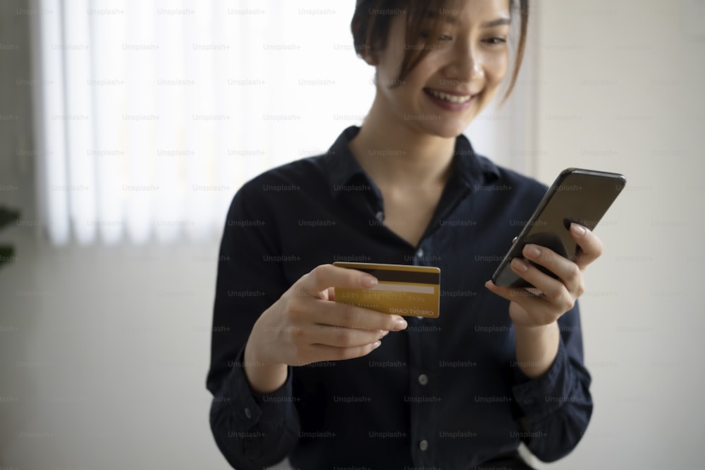 Smiling young woman holding credit card paying bills online or shopping online with smart phone.