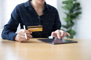 Ausschnittaufnahme einer jungen Frau, die eine Kreditkarte hält und ein digitales Tablet benutzt, um Rechnungen online zu bezahlen oder online einzukaufen.