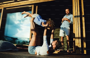 Happy family with small daughter having fun on patio of wooden cabin, holiday in nature concept.