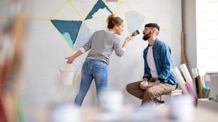 Mid adults couple having fun when painting wall indoors at home, relocation and diy concept.