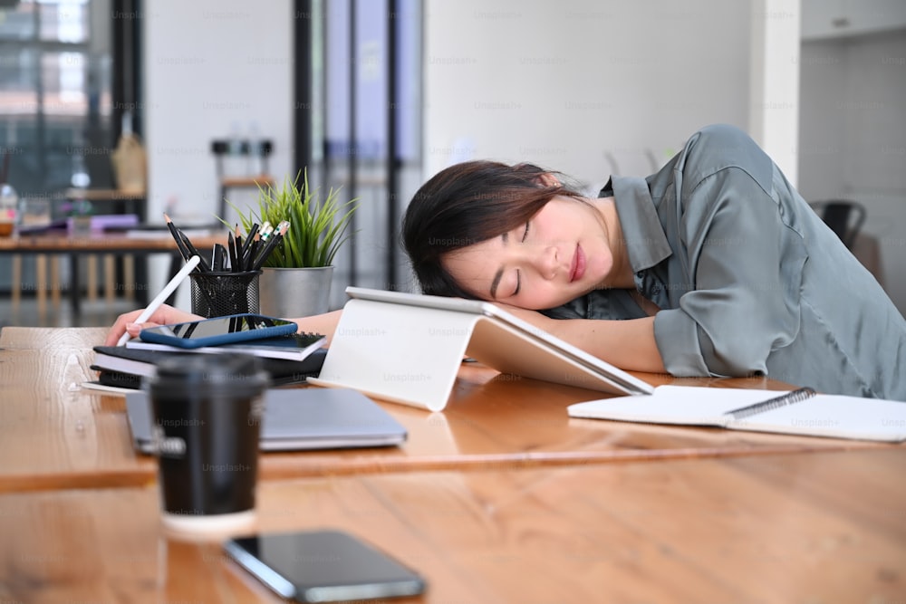 Giovane impiegata stanca che fa un pisolino alla scrivania del suo ufficio.