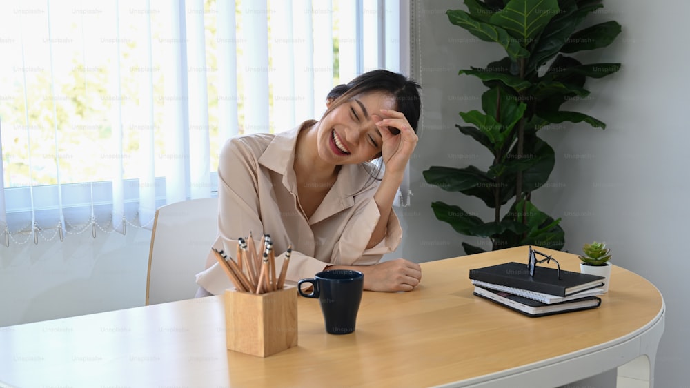 Cheerful businesswoman laughing and sitting at her workplace in office.