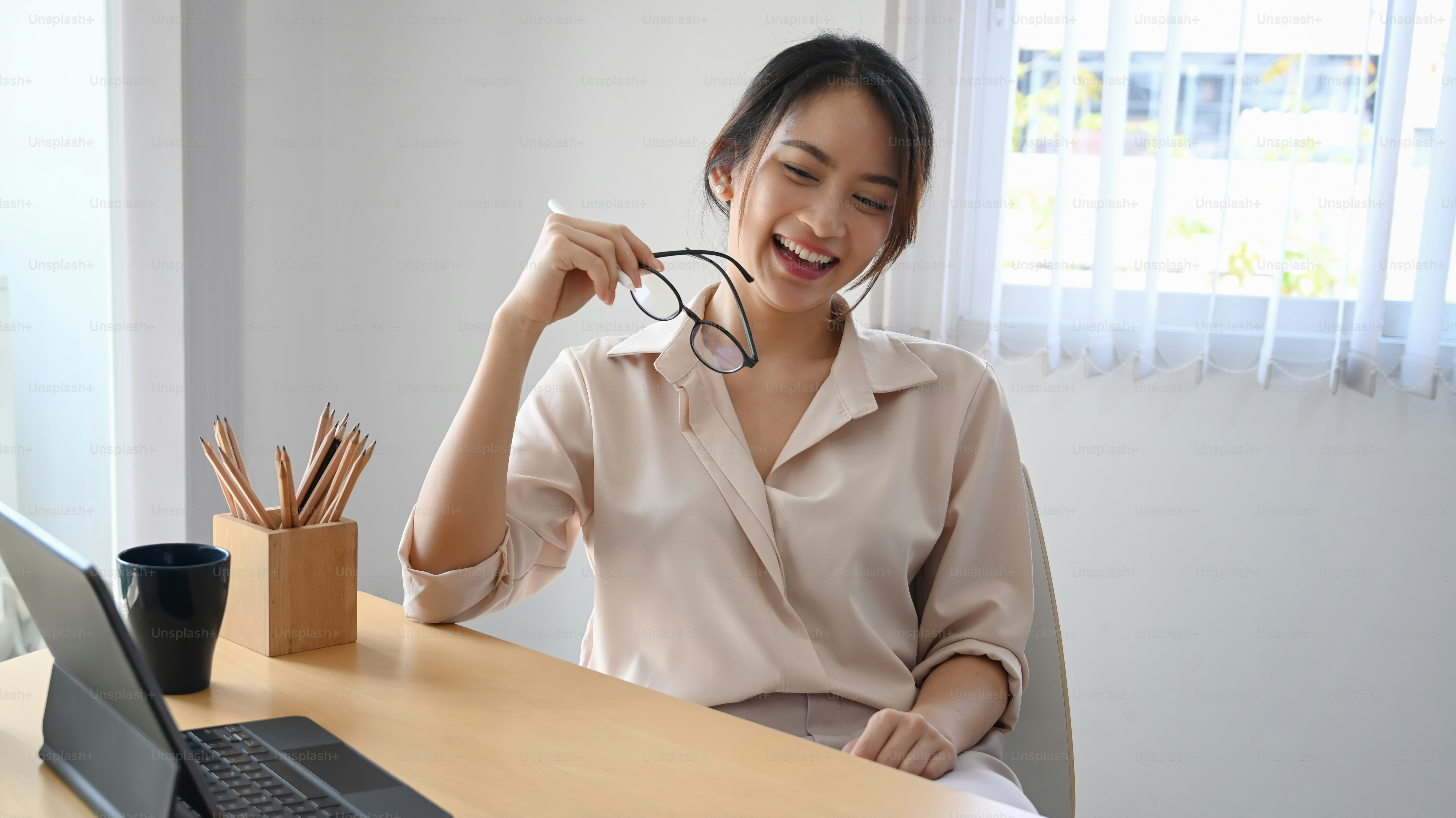Happy woman office worker holding her glasses and smiling while sitting at her workplace