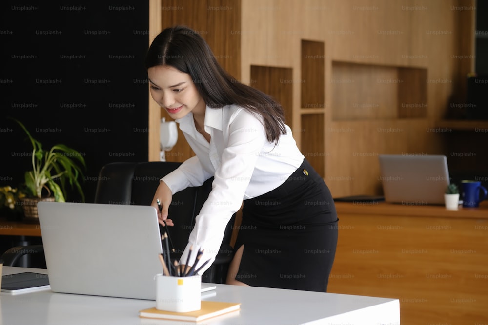 Happy businesswoman standing at her workplace and reading email on laptop computer.