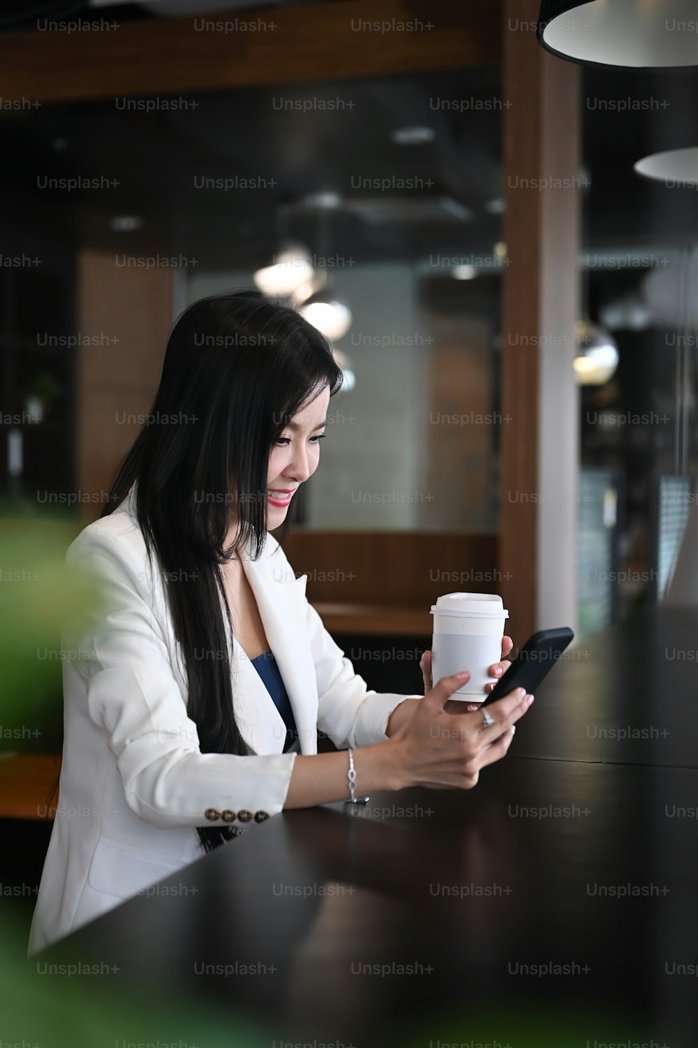 Angenehme Unternehmerin, die in einem modernen Büroladen sitzt und das Smartphone benutzt.