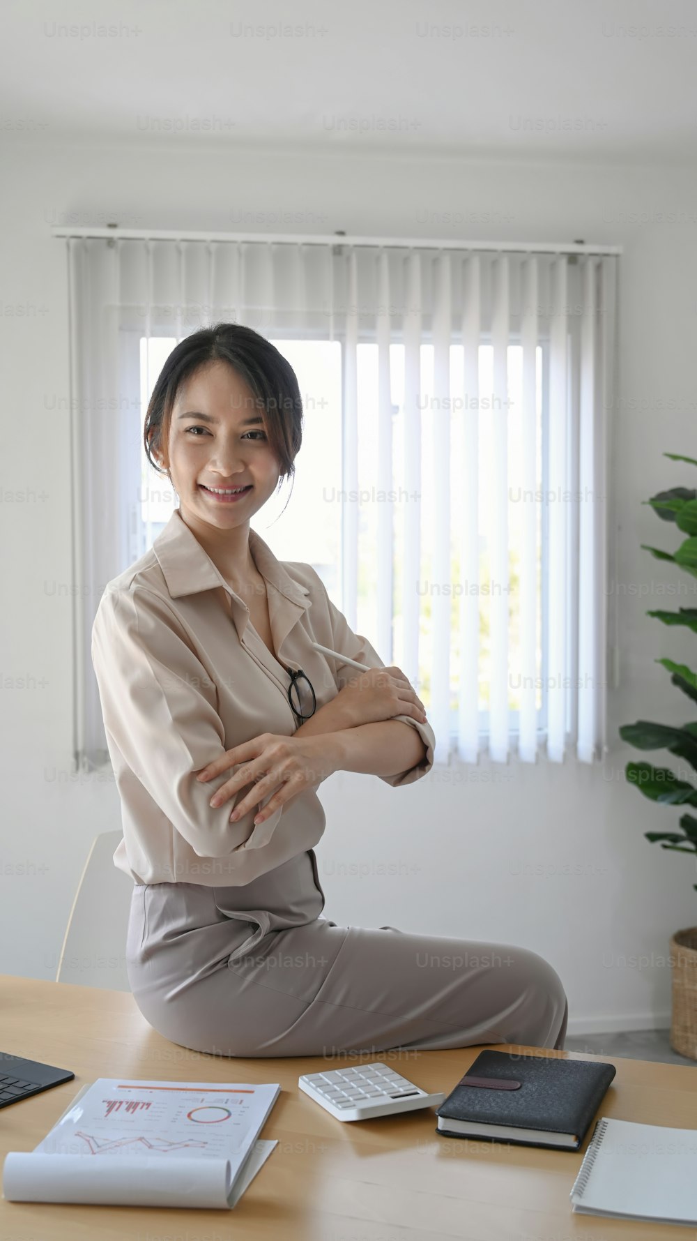 Portrait of confident businesswoman sitting on her desk with arms crossed and looking at camera.