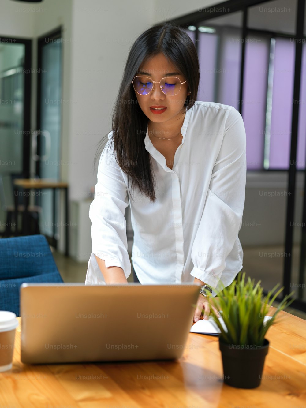 Portrait of female worker standing and working with laptop on wooden table in office room