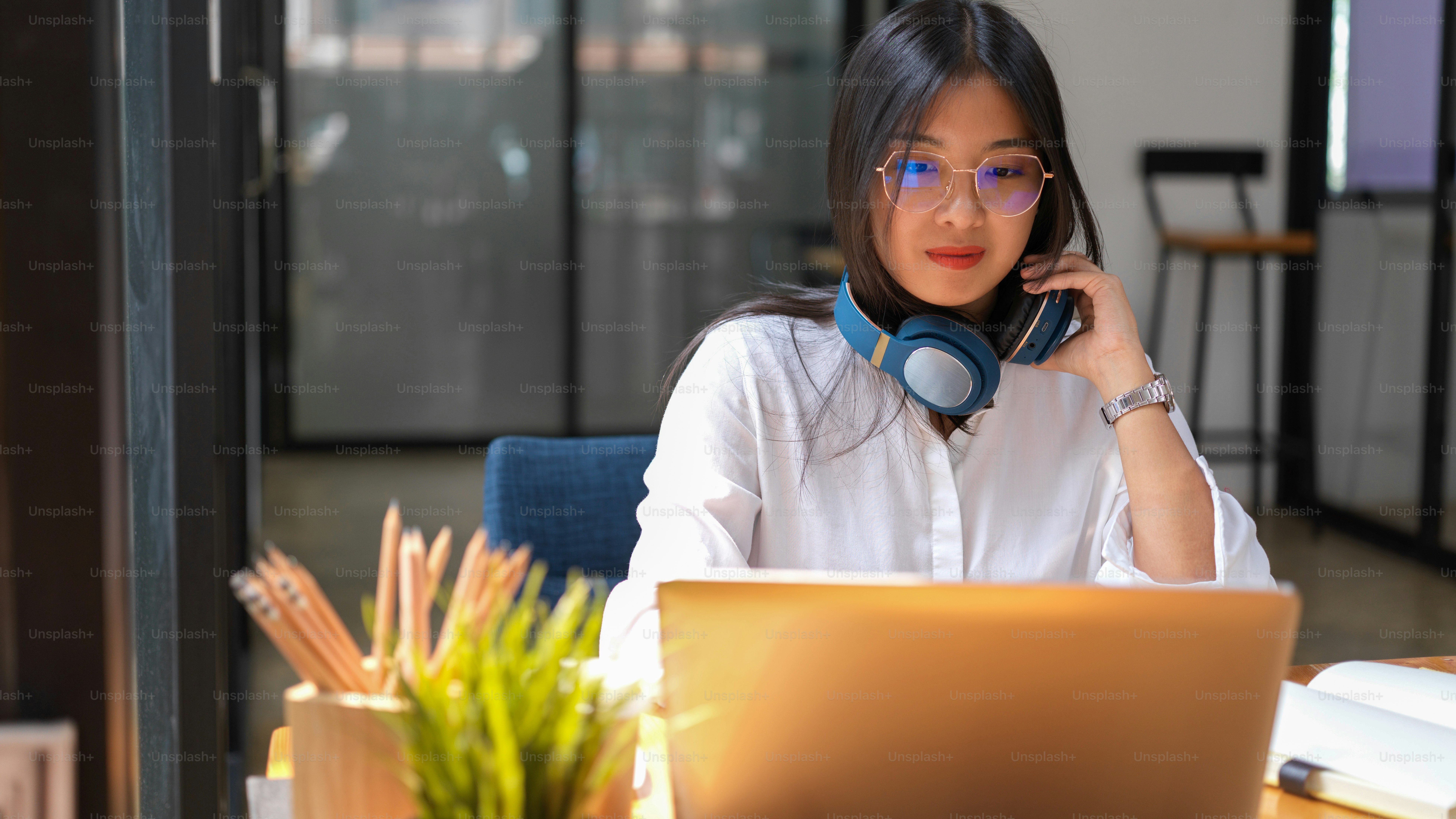 Half-length portrait of young female with headphone working with laptop and supplies in library