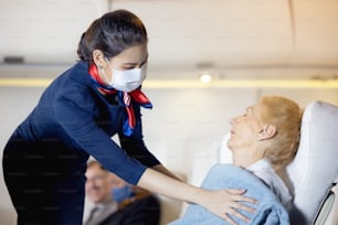 A female flight attendant clothed an elderly passenger sleeping in the passenger seat. Stewardess taking care of the passenger. Cabin crew gives service to a passenger in an airplane.