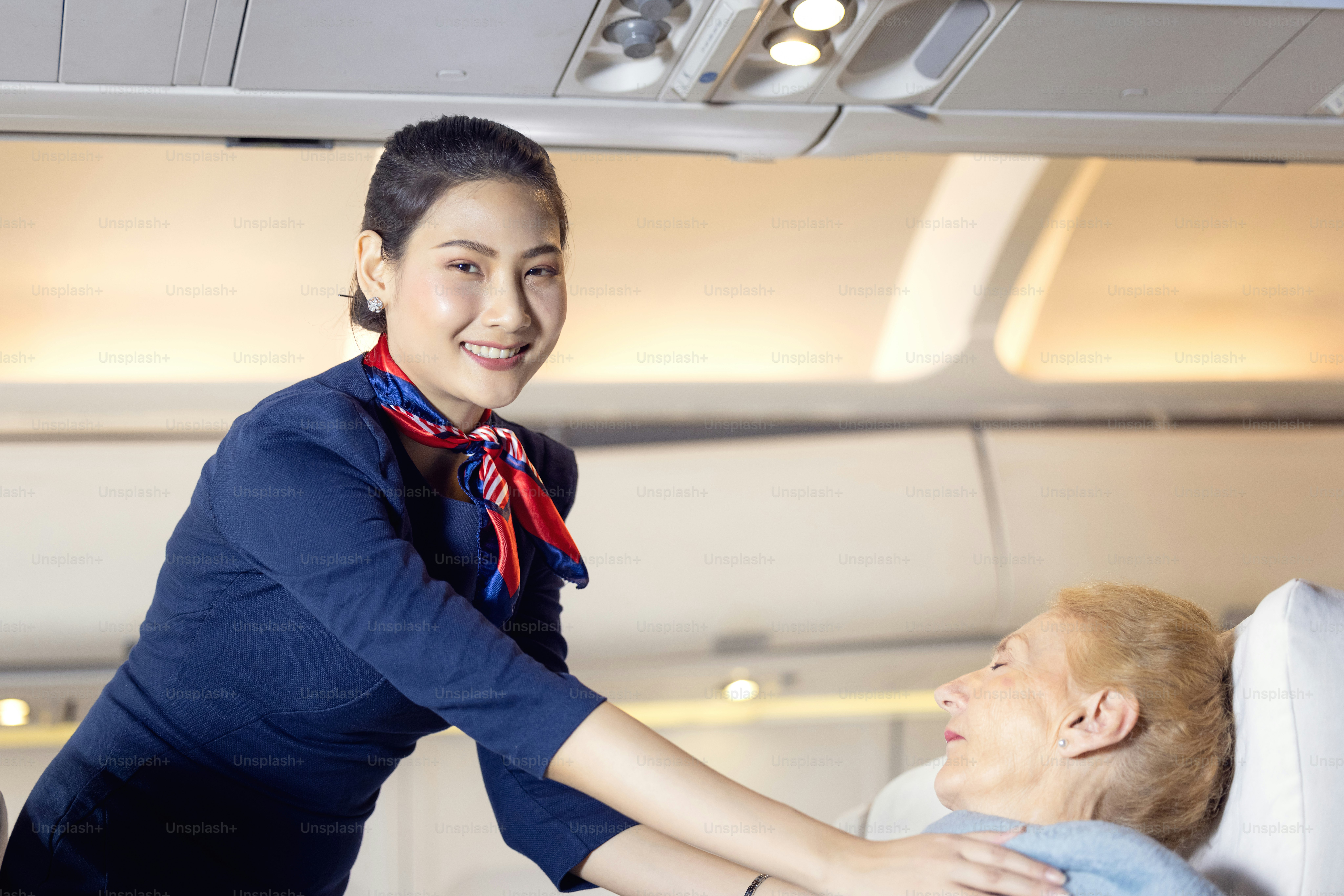 A flight attendant in a blue uniform adjusting a blanket for a passenger
