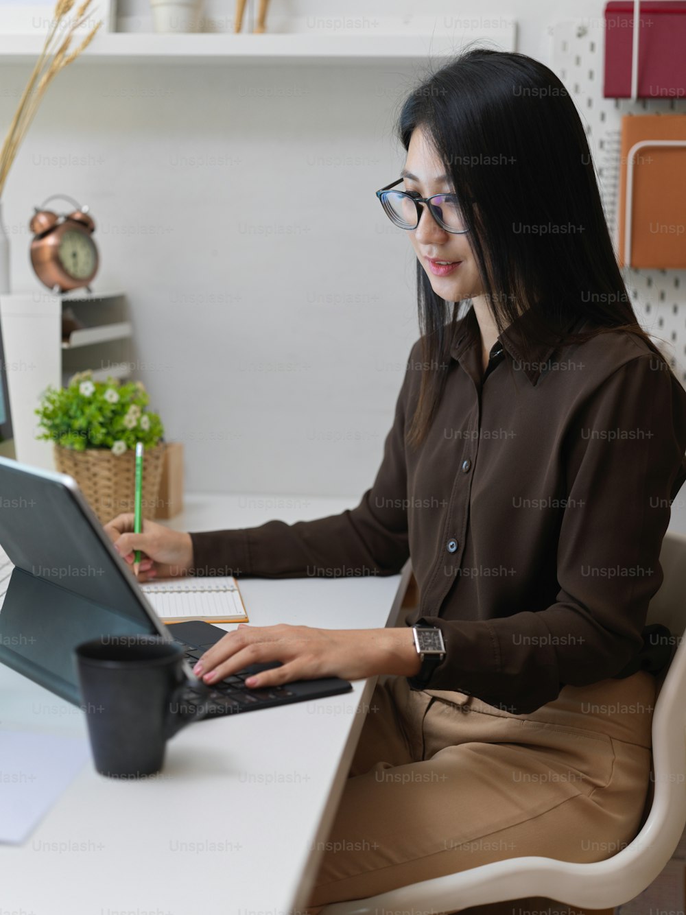 Ausschnittaufnahme einer Büroangestellten bei der Arbeit mit einem digitalen Tablet in einem modernen Büroraum