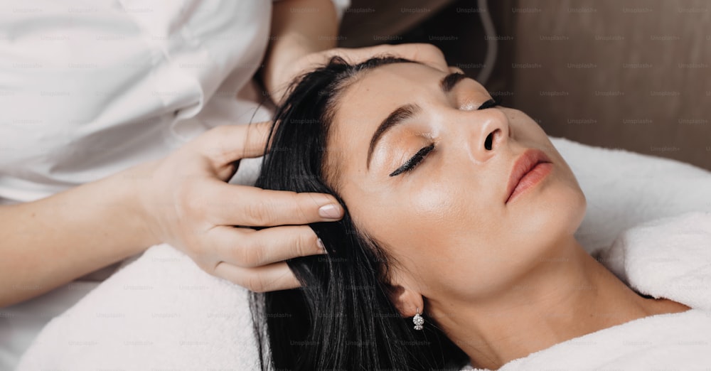 Foto de primer plano de una sesión de masaje de cabeza realizada en el centro de spa a una mujer morena acostada con los ojos cerrados