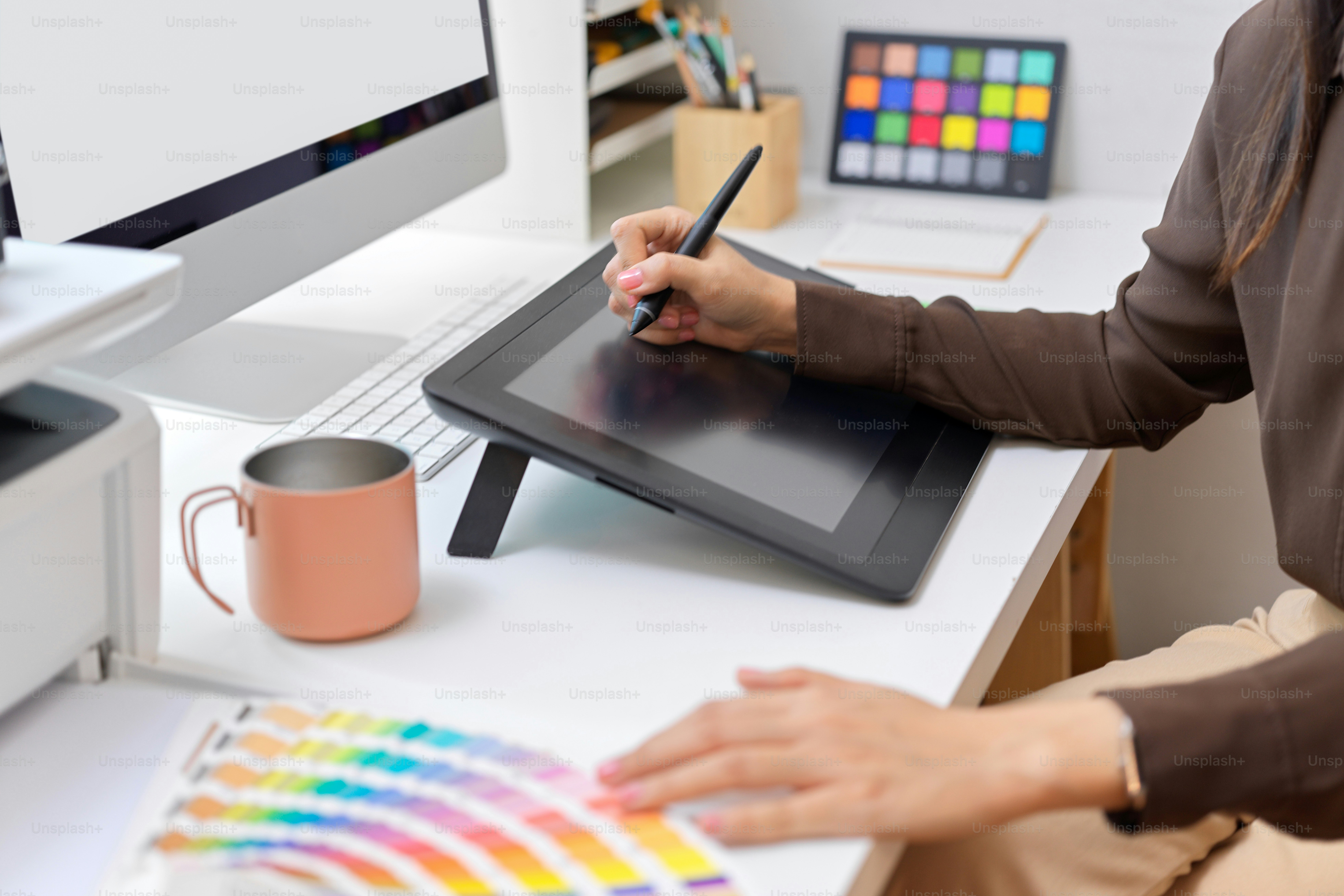 Vue latérale d’une main de designer féminine travaillant avec une tablette à dessin et un échantillon de couleur sur un bureau d’ordinateur