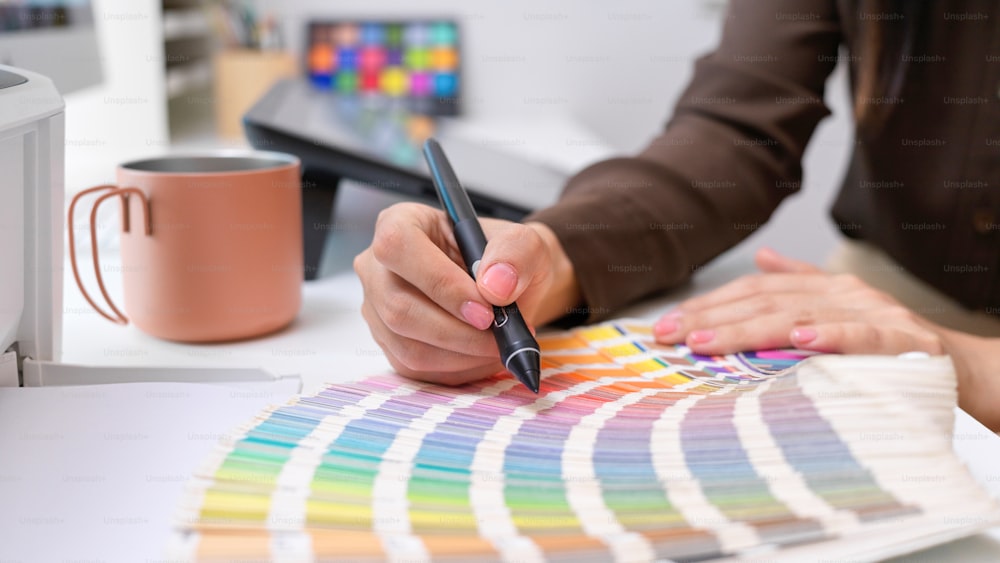 Close up view of female designer choosing colour on colour swatch on computer desk in office room