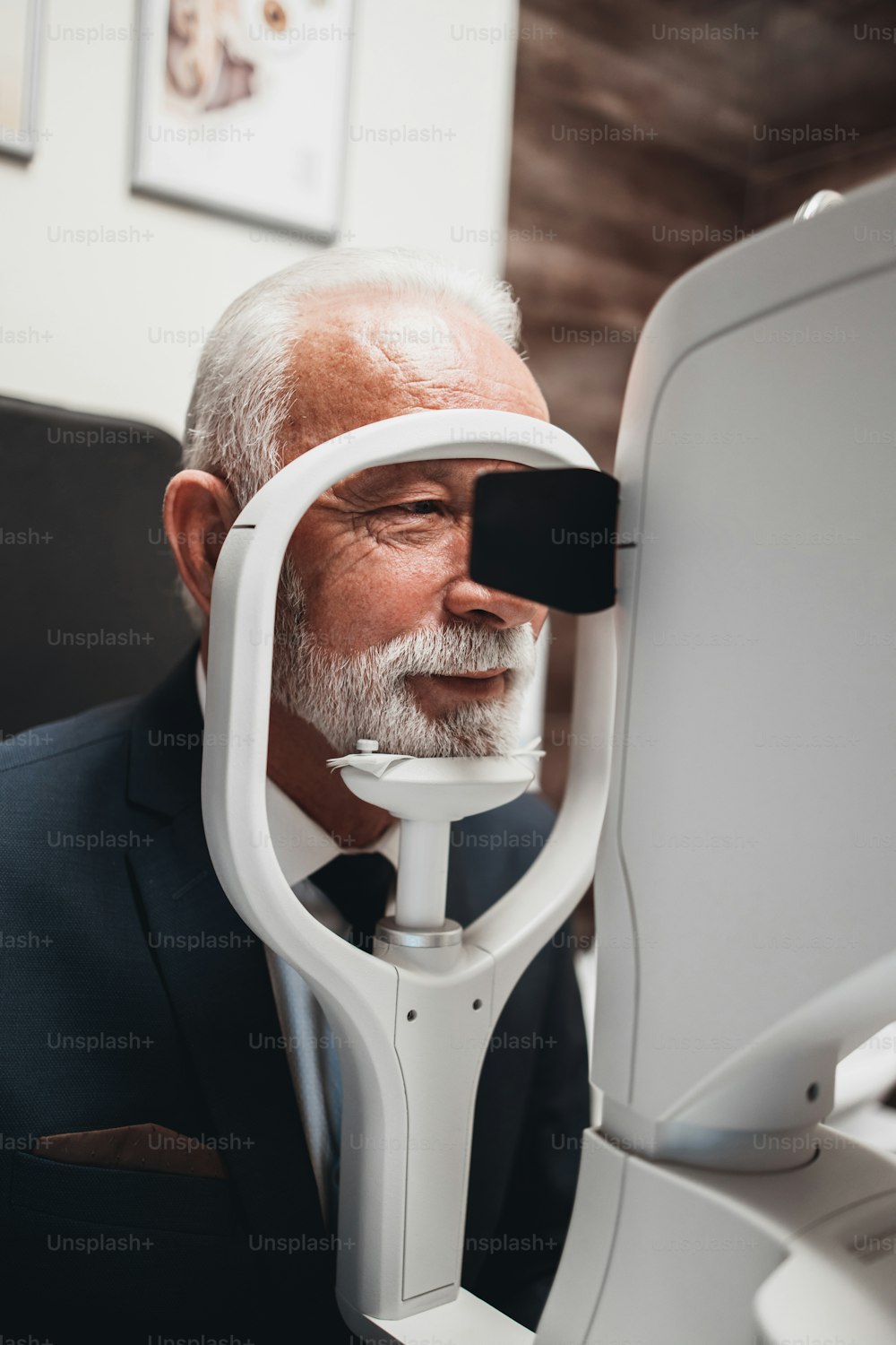 Elegant senior bearded man receiving ophthalmology treatment. Doctor ophthalmologist checking his eyesight with modern equipment.