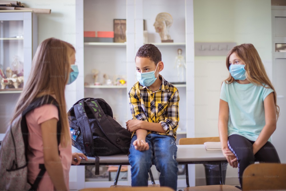 Conversation before class. Small group of school children in classroom talking. With face mask.