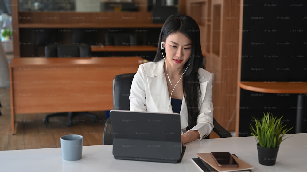 Confident businesswoman working with computer tablet and listening music over earphones at office.