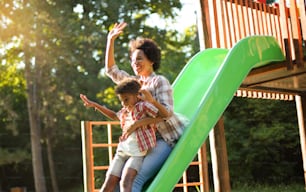 African American mom playing with child on playground. Fun on toboggan.