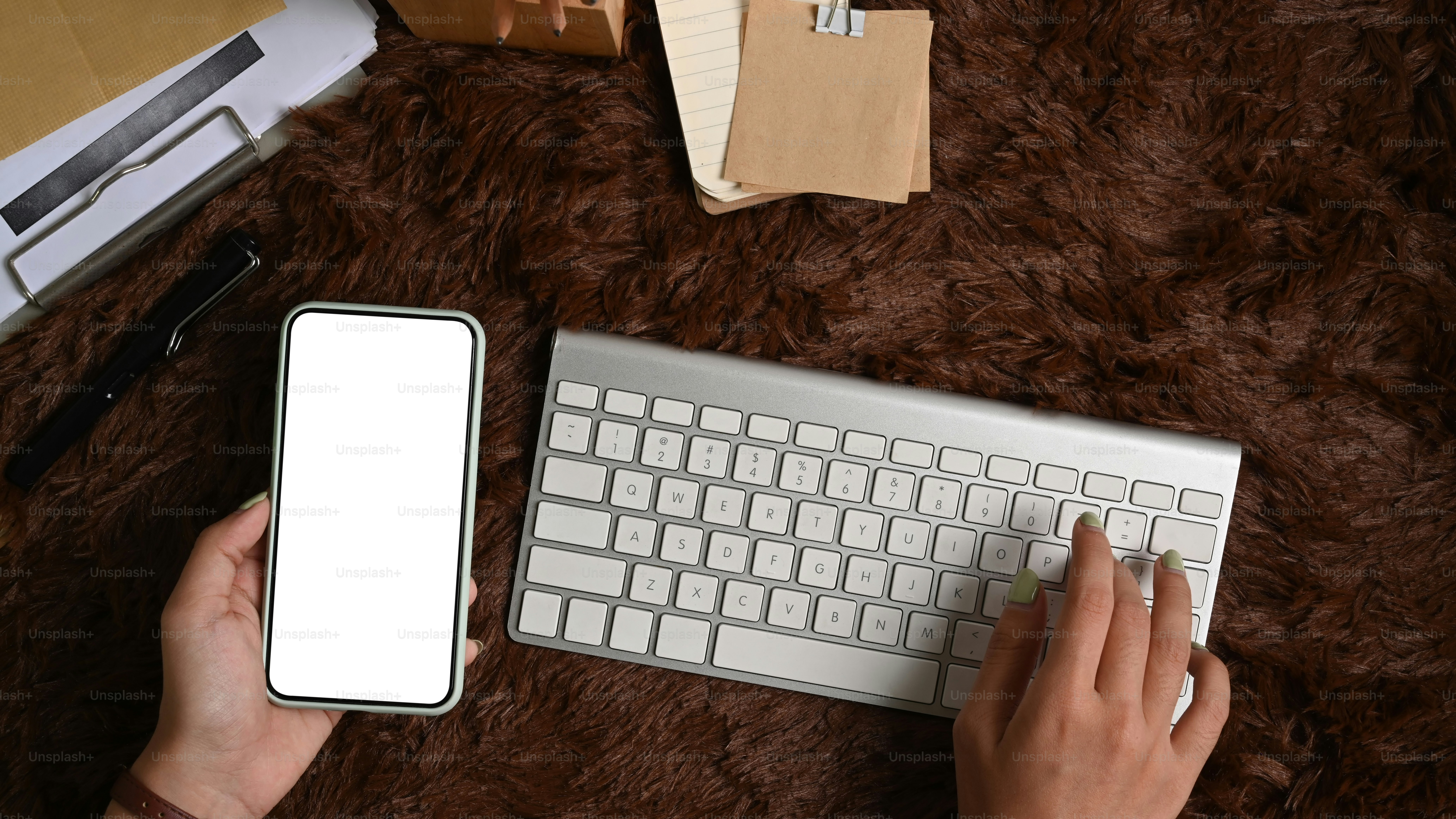 Hight view of woman hand holding smart phone and typing on keyboard over brown fur rug.
