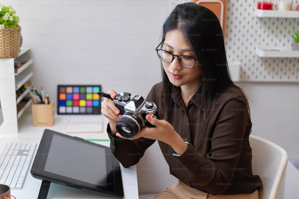 デザイナー用品とオフィスの机に座っている間、カメラで作業する女性デザイナーの肖像画