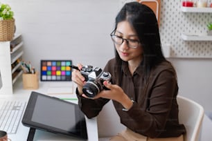 Porträt einer Designerin, die mit der Kamera arbeitet, während sie mit Designerbedarf am Schreibtisch sitzt
