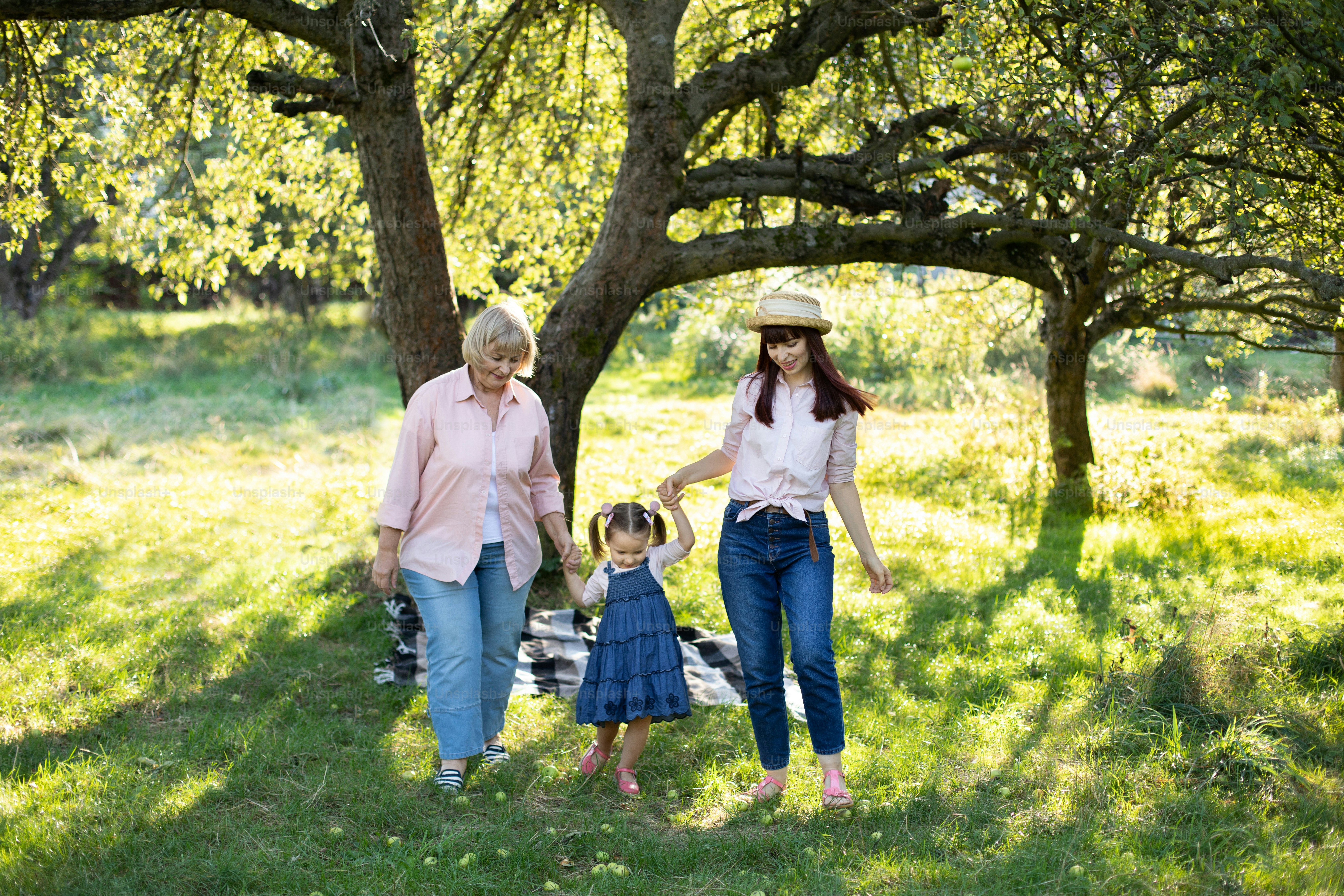 Three generation family, pleasan senior lady, young mom and little cute three years old girl, walking outside in the nature green park, holding hands and smiling.