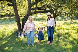 Momenti di unione familiare, rapporto felice tra generazioni diverse. Ritratto di famiglia multigenerazionale femminile, che cammina fuori nel giardino soleggiato estivo e si diverte.