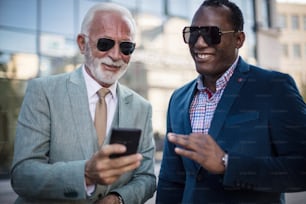 Business men standing on street and using smart phone. Focus is on men.