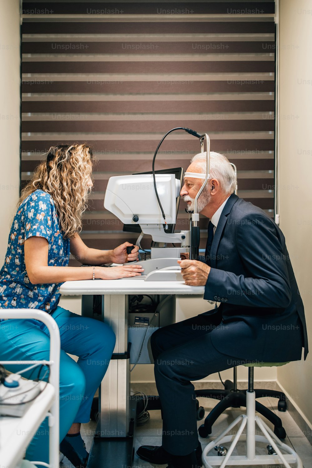 Elegant senior bearded man receiving ophthalmology treatment. Doctor ophthalmologist checking his eyesight with modern equipment.