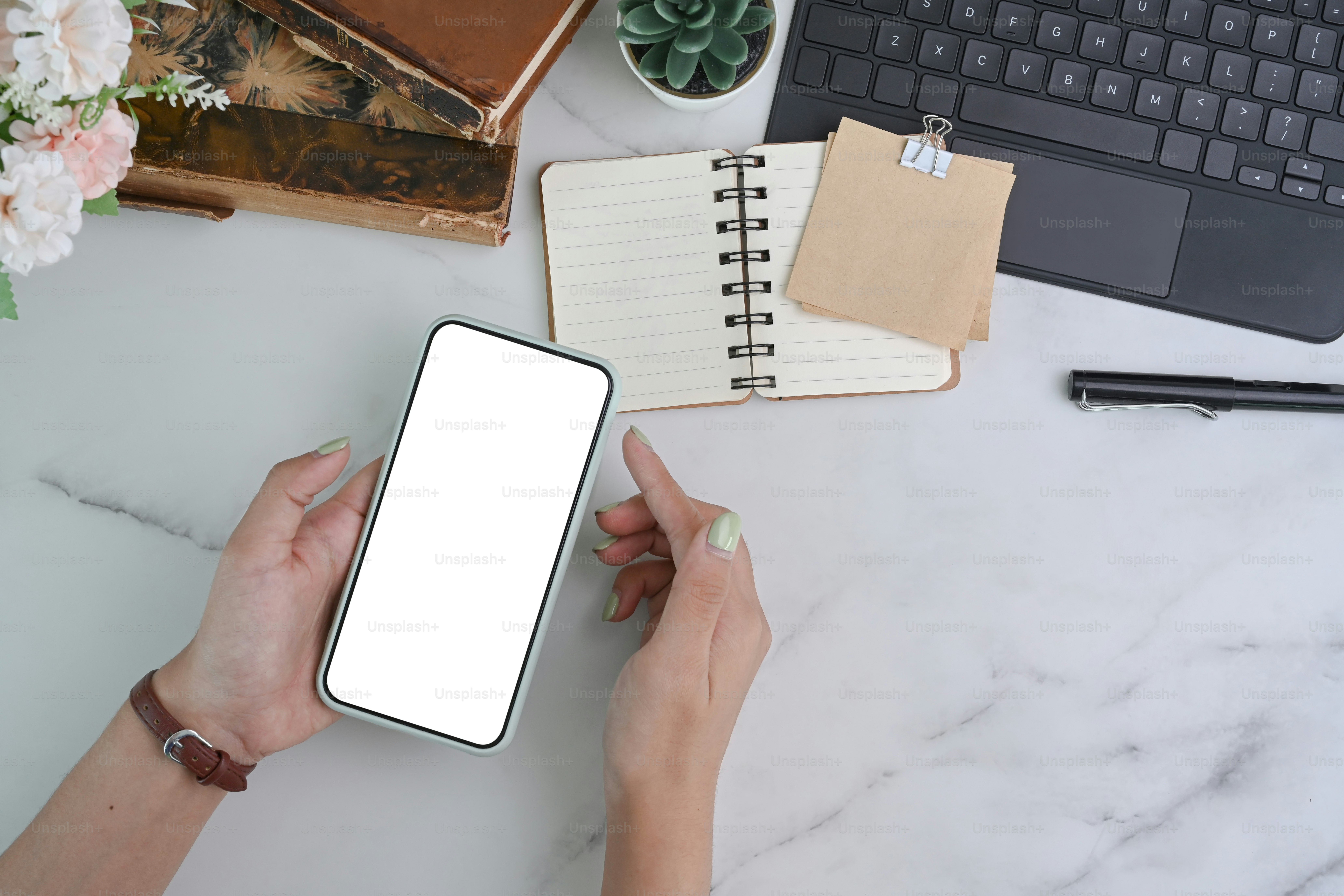 Top view of young woman holding mock up smart phone with blank screen over marble table.