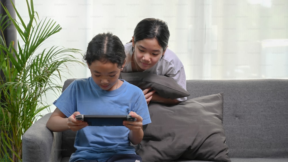 거실에서 게임을 하는 여동생을 보고 있는 젊은 아시아 소녀.