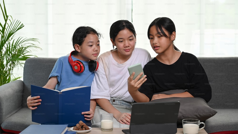 세 명의 어린 소녀들이 소파에 앉아 스마트폰으로 무언가를 보고 있다.