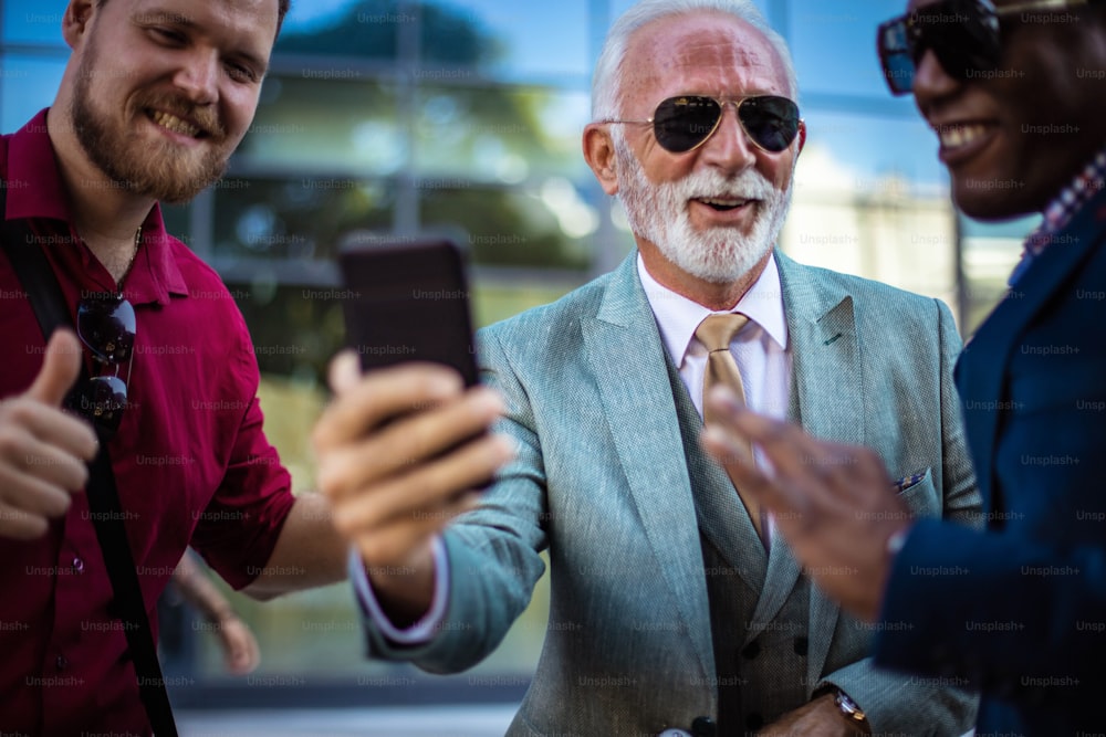 Colegas de negocios que usan el teléfono móvil al aire libre en la ciudad. La atención se centra en el hombre mayor. De cerca.