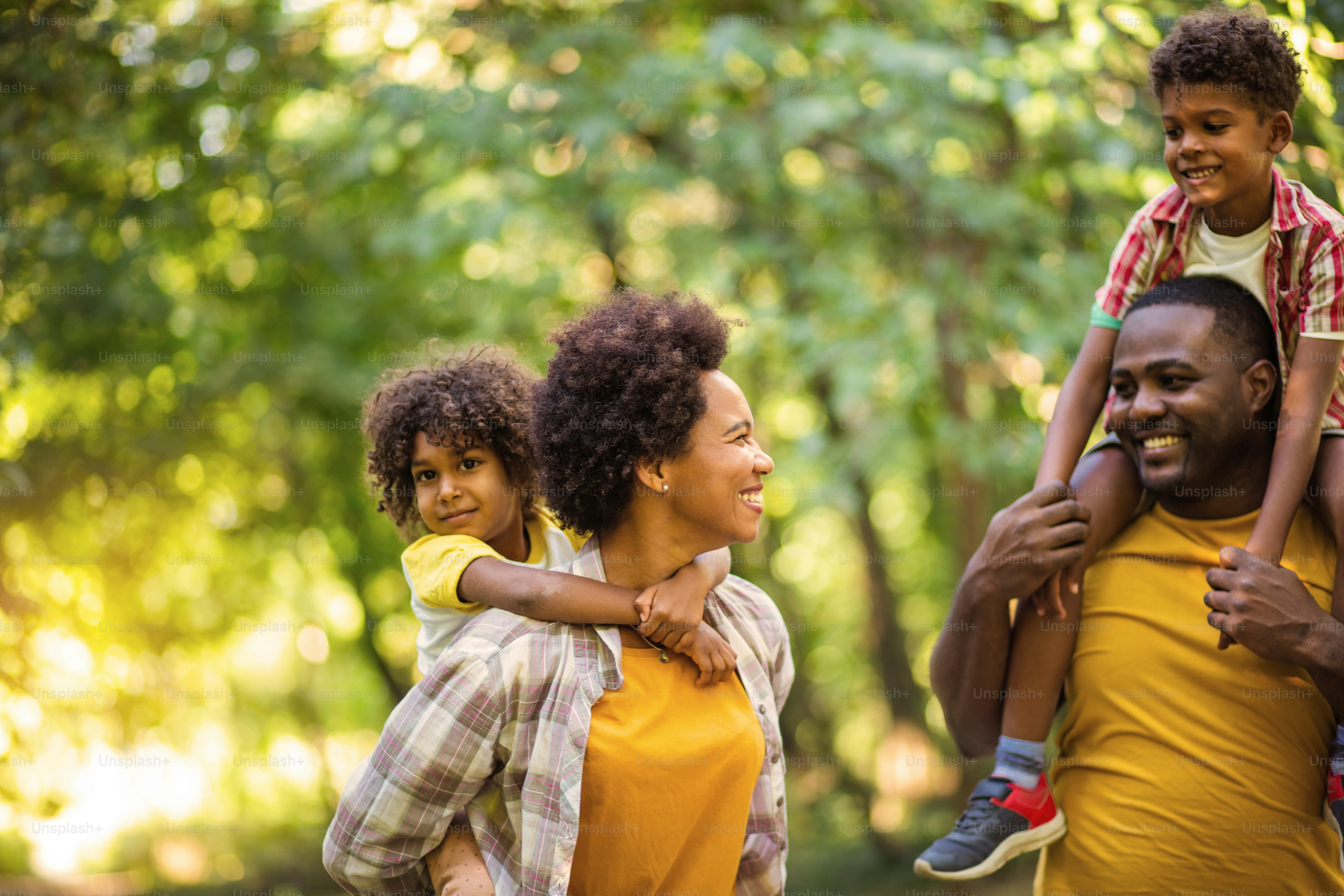 African American family walking trough park. Parents carrying children on  piggyback. photo – Family Image on Unsplash, image size:3000x2000