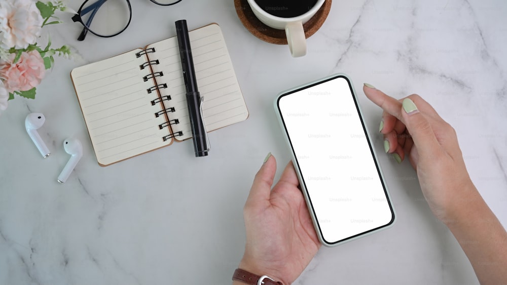 Hand of woman holding mobile phone with blank screen on marble background.