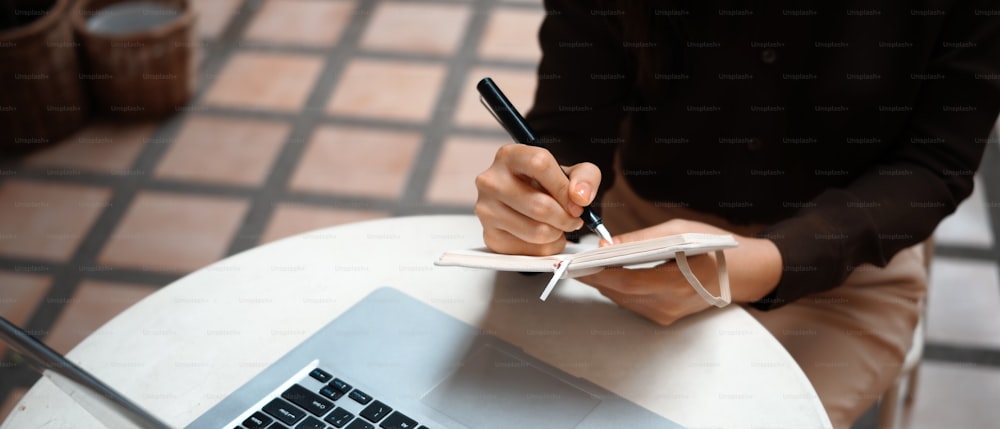Foto cortada de uma jovem mulher segurando caneta escrevendo no dia de trabalho de planejamento do caderno.
