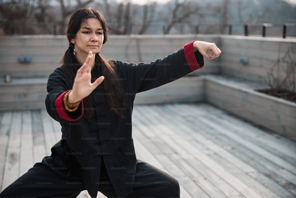 Woman standing firmly on bent legs while pressing fingers of left hand to thumb and reaching ahead with right arm