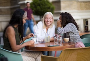 Three women sitting in café on street and talking. Focus is on two women.