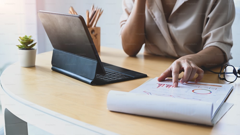 Ausschnittaufnahme einer Geschäftsfrau, die mit einem Computer-Tablet arbeitet und Finanzberichte am Schreibtisch analysiert.