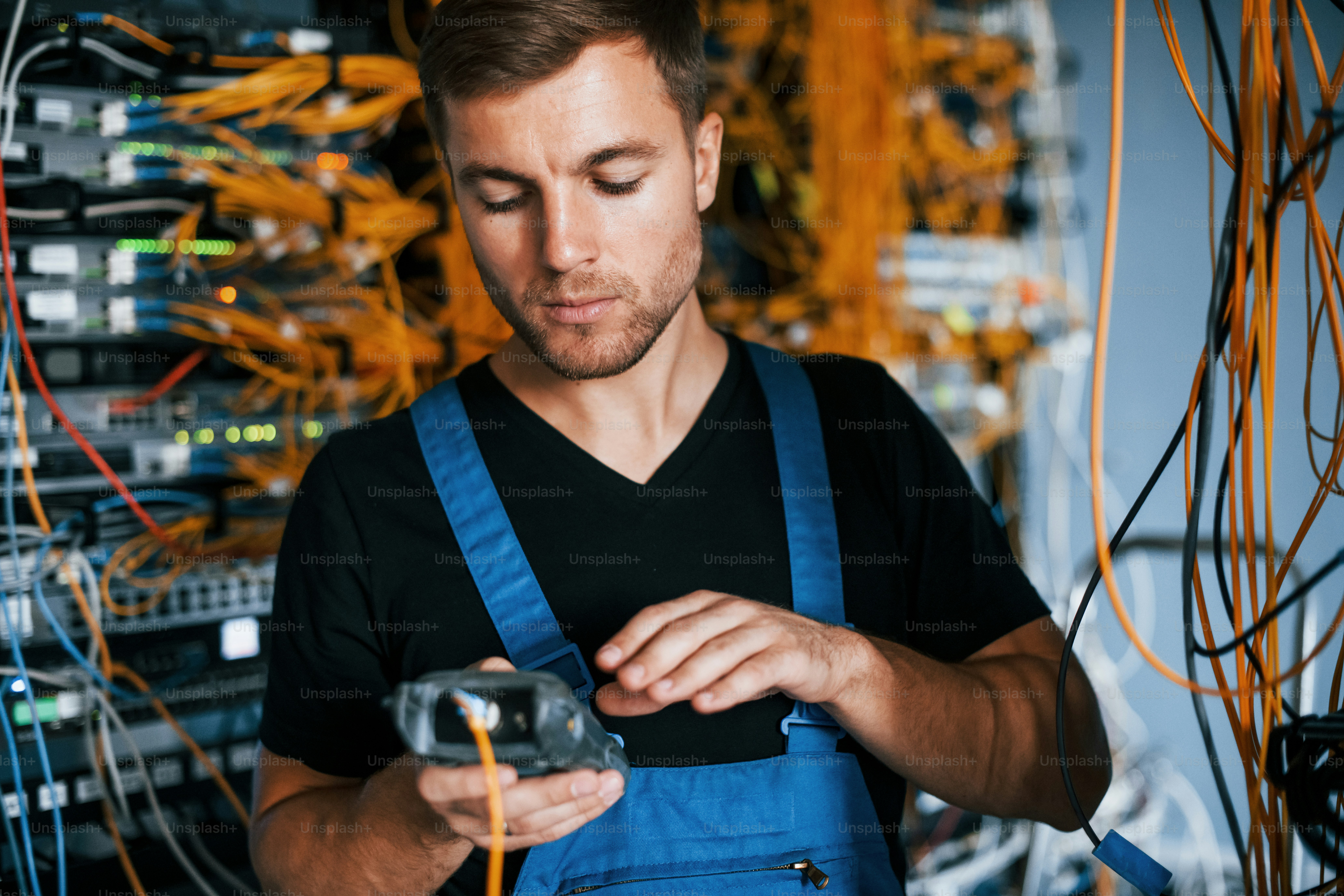 Junger Mann in Uniform hat einen Job mit Internetgeräten und Kabeln im Serverraum.