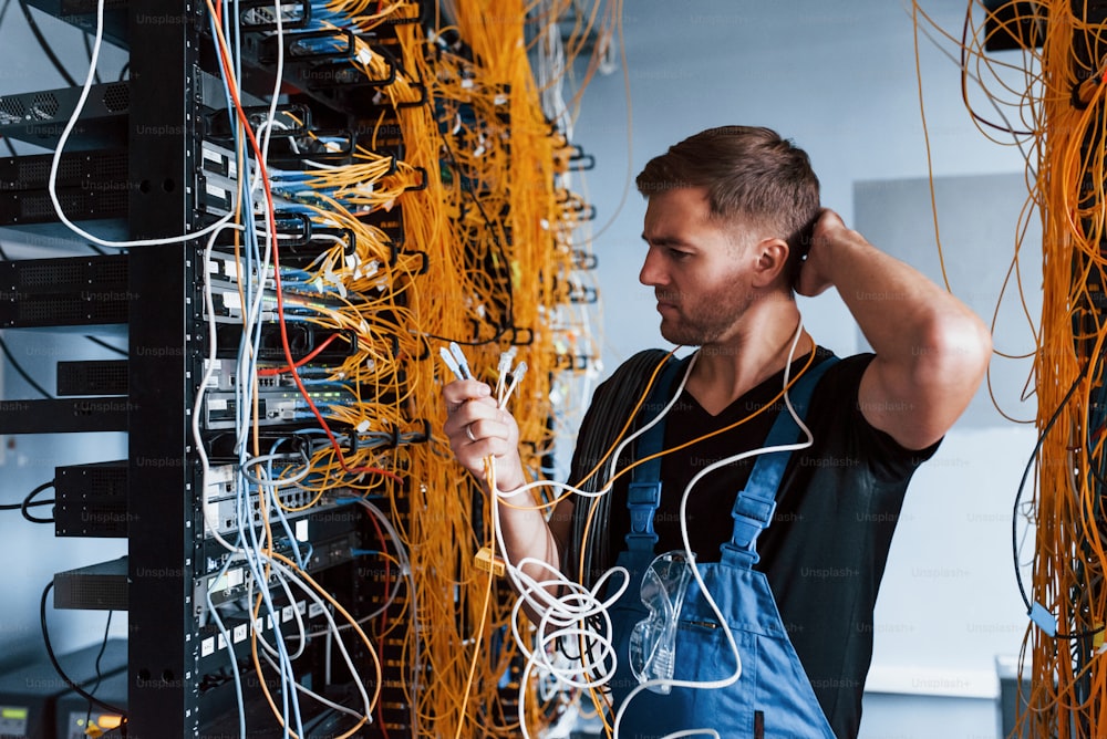 Un joven uniformado se siente confundido y busca una solución con el equipo de Internet y los cables en la sala de servidores.